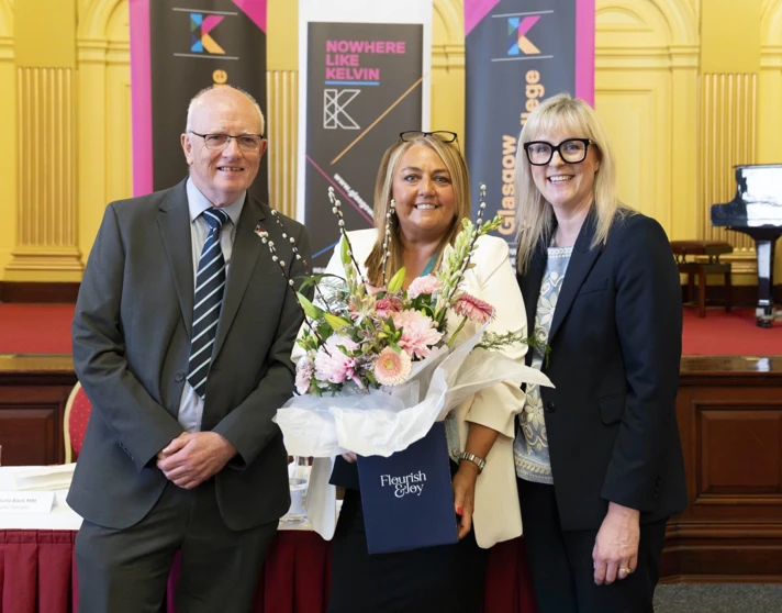 Three people smiling at Glasgow Kelvin College awards event, with one woman holding a bouquet of flowers. Three people smiling at Glasgow Kelvin College awards event, with one woman holding a bouquet of flowers.